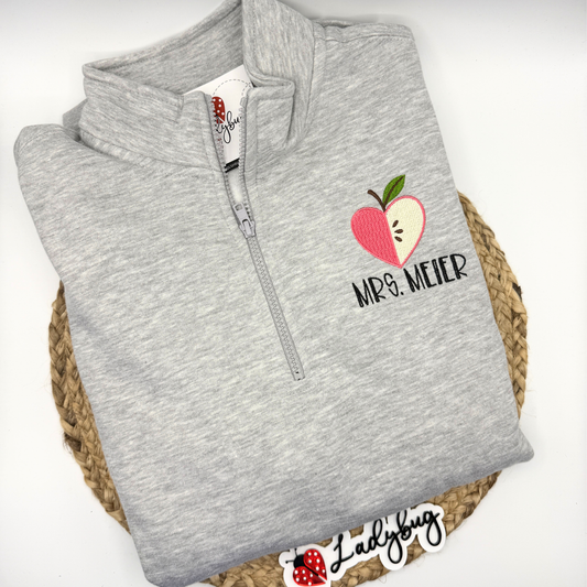 Personalized teacher quarter zip with embroidered name and apple heart design
Close-up of apple heart embroidery with teacher name underneath
Teacher wearing custom embroidered quarter zip sweatshirt